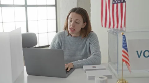Woman typing on laptop at a voting table with clear ballot box, sticker she.. Stock Footage 337434439