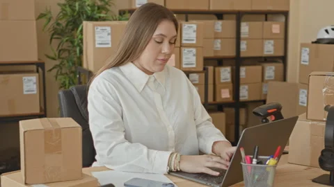 Woman typing on laptop while packing parcels with visible hands at a shippi.. Stockbeeldmateriaal 337393581