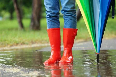 Woman with umbrella and rubber boots in puddle, closeup. Rainy weather Stock Photos
