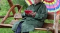 Woman with umbrella sits on the swing bench and uses smartphone HD Footage