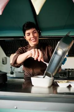 Woman in uniform smiling while preparing food in the kitchen of her small food Stock Photos