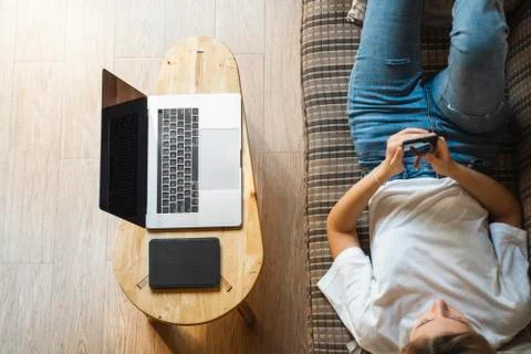 Woman use a smartphone while lying on a sofa with a laptop and ereader on a Stock Photos
