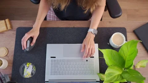Woman uses computer mouse and types on laptop keyboard at home desk with coffee Stock Footage 346780612