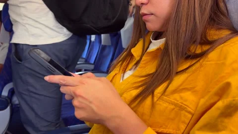 A woman uses her smartphone while seated in an airplane. Modern travel setting Stock Footage 307570942