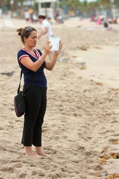 Woman uses tablet computer to capture family images on beach Foto stock