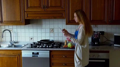 Woman uses a tablet computer in the kitchen and cooks. Stock Footage 73719221