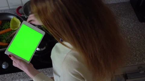 Woman uses a tablet computer in the kitchen and cooks . Top view. Green screen. Stock Footage 73724818