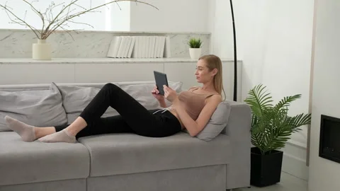 A woman uses a tablet while lying on the sofa at home. Stock Footage 253723704