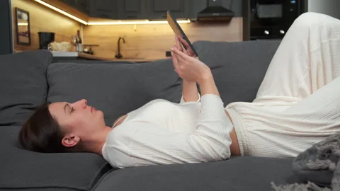 A woman uses a tablet while lying on a sofa at home. Stock Footage 301661535