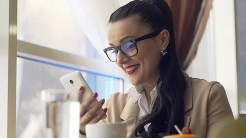 Woman using app on smartphone in cafe drinking coffee smiling and texting on Vídeo Stock 73416429