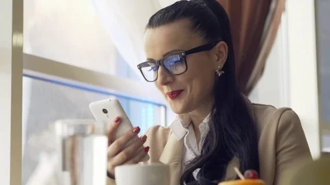 Woman using app on smartphone in cafe drinking coffee smiling and texting on 스톡 동영상 73416564