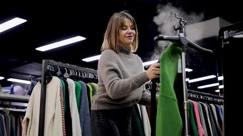 Woman using a clothes steamer and ironing a green jumper in a clothes shop Stock Footage 303304647