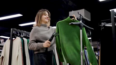 Woman using clothes steamer on wool sweater in modern clothing store Stock Footage 303304648