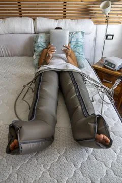 Woman using compression therapy machine for legs at home Stock Photos