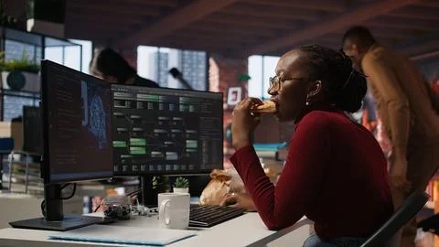 Woman using computer in artificial intelligence development agency, eating food 스톡 사진
