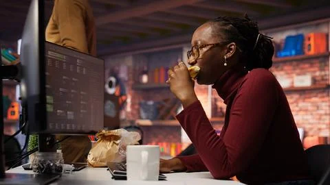 Woman using computer in artificial intelligence development agency, eating food Stock Photos