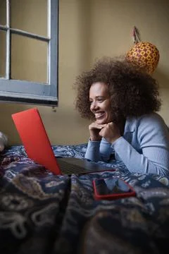 Woman using a computer laptop while lying on a bed at home. Stock Photos