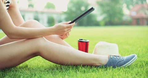 Woman using digital tablet computer sitting in the park, on a lawn. Slow motion Vidéo 53104164