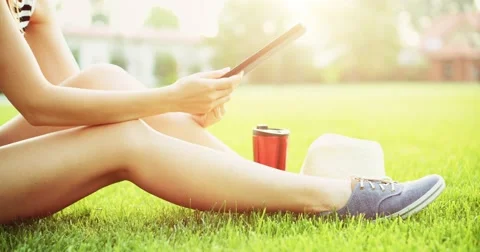 Woman using digital tablet computer sitting in the park, on a lawn. Slow motion 스톡 동영상 66855492