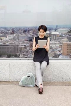 Woman using a digital tablet, with her back tyo the view over a large city. Stock Photos