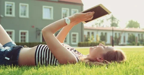 Woman using digital tablet lying on the green grass. Slow motion. Lens flare. Video stock 53106707