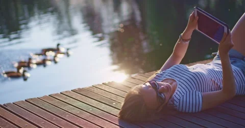 Woman using digital tablet outdoors, relaxing on a wooden jetty near the lake 스톡 동영상 51069647