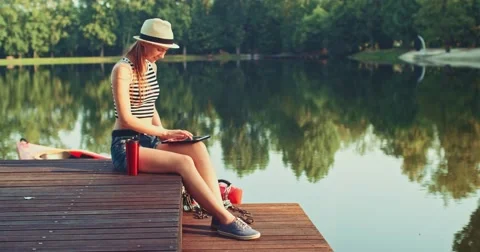 Woman using digital tablet sitting on a wooden jetty by the lake. Slow Motion. Vidéo 53112199