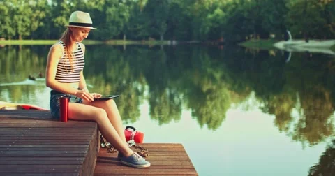 Woman using digital tablet sitting on a wooden jetty by the lake. Slow Motion. Vidéo 53112729