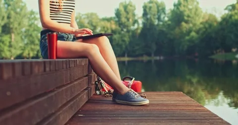 Woman using digital tablet sitting on a wooden jetty by the lake. Slow Motion. Vidéo 53113144
