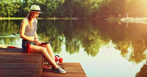 Woman using digital tablet sitting on a wooden jetty by the lake. Slow Motion. Stock-Footage 66856352