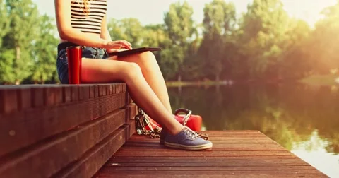 Woman using digital tablet sitting on a wooden jetty by the lake. Slow Motion. Vidéo 66856410