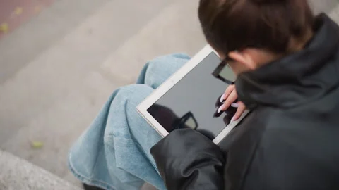 Woman using digital tablet while seated outdoors in natural daylight wearing Stock Footage 347978974