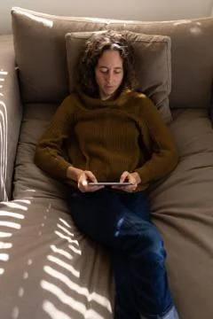 Woman using digital tablet while laying on the couch at home Stock Photos