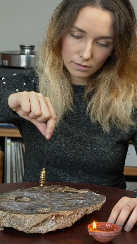A woman using a dowsing pendulum over a big agate stone. Stock Footage 331290627