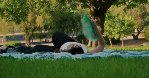 Woman using a fan in a park Stock Footage 341773574