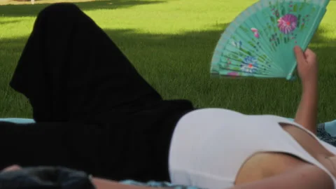 Woman using a fan in a park Stock Footage 341773685