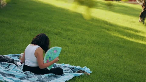 Woman using a fan in a park Stock Footage 341773688