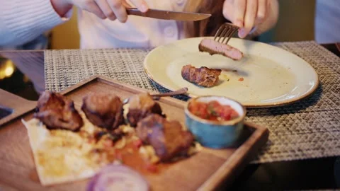Woman using fork and knife to eat grilled beef meat skewers on wooden board.. Vídeos de archivo 339783610