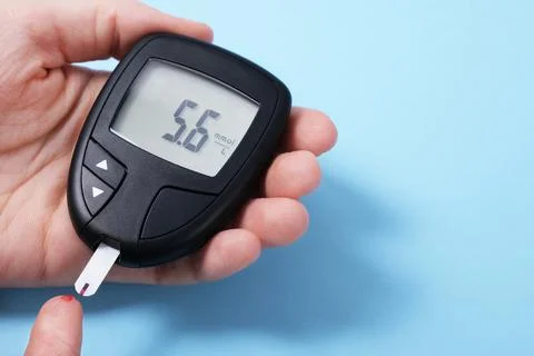 Woman using glucometer, checking blood sugar level. Diabetes concept on blue Foto stock