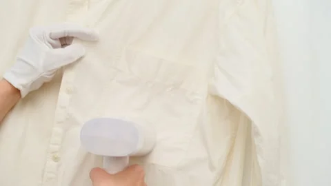 Woman using handheld garment steamer to remove wrinkles from shirt. Housekeeping Stock Footage 344906364