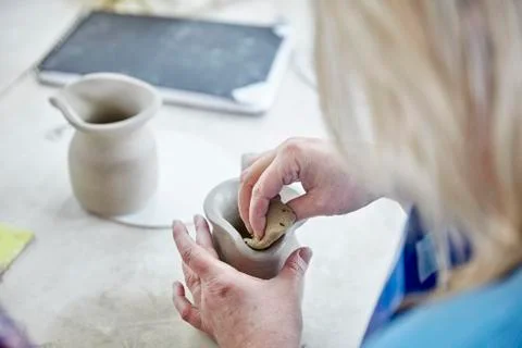 A woman using her hands to shape and smooth a wet clay jug to match another, Foto stock