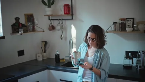 A woman using her phone while standing at the kitchen. Stock Footage 234394367