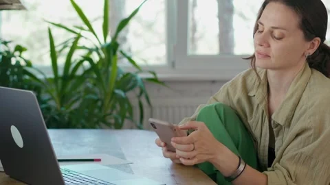 A woman using her phone while sitting in front of a laptop Video stock 285216659