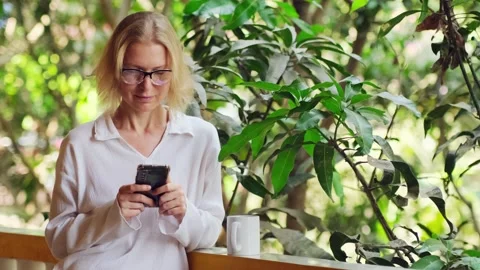 Woman is using her smartphone, drinking morning coffee on the balcony. Stock Footage 240193463