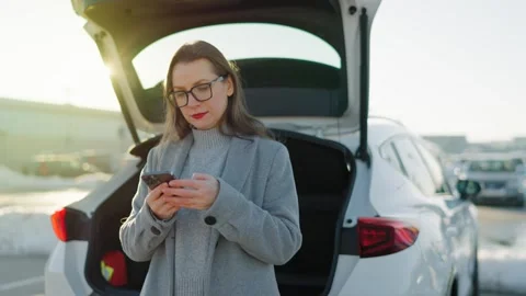 Woman is using her smartphone while standing by a car during the winter season Stock Footage 301542184