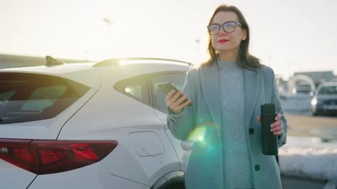 Woman is using her smartphone while standing by a car during the winter season Stock Footage 302842884