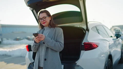 Woman is using her smartphone while standing by a car during the winter season Stock Footage 304008537