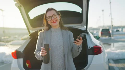 Woman is using her smartphone while standing by a car during the winter season Stock Footage 304008831