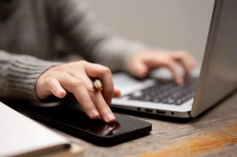A woman using her smartphone while typing on a keyboard, working on her lap.. Foto stock