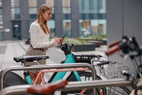 A woman is using her smartphone while she stands at a bicycle rack in an urban Stock Photos